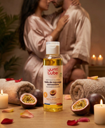 Couple enlacé en peignoirs de satin, flacon d'huile de massage Passion au premier plan avec des fruits de la passion et des bougies